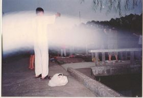 '图一:一九九八年七月二十九日清晨,拍摄于湖南大学图书馆旁的法轮功炼功点,学员们正在炼第二套功法的“头前抱轮”动作。当日为阴天,照片中清晰可见巨大的银白色光束(能量罩),笼罩着整个炼功点'