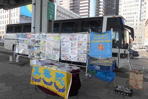 '真相展板后面是大陆游客大巴。参观完自由女神像回来的游客在此集合，他们边等人边看真相。右边蓝色小推车，每天将这里的真相条幅、资料收纳整齐。退<span