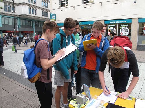 '图6:一组在附近一所学院学摄影、艺术和数学的学生在卡迪夫(Cardiff)商业中心长时间驻足听法轮功学员讲真相,随后一一签名反对中共“活摘”罪行,其中一个叫布鲁斯的高个子告诉法轮功学员他坚决反对共产党。'