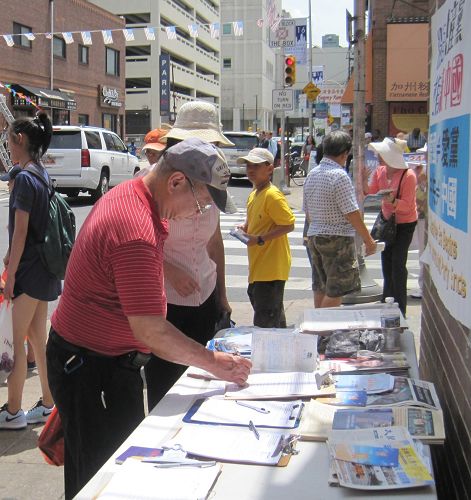 '图8：费城居民朱先生被法轮功学员在集会上演唱的歌曲《你我有缘》深深地打动，并在征签表上签名。'