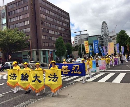 '图1~2:八月五日(星期六),法轮功学员们从早上七点开始在爱知县名古屋市中心的荣公园(Sakae Park)炼五套功法,之后在最繁华地区的荣(Sakae)举办游行。游行队伍由精神抖擞的天国乐团引领,其后是打着“法轮大法好”、“真善忍”、“呼吁停止迫害法轮功”等横幅的队伍。'