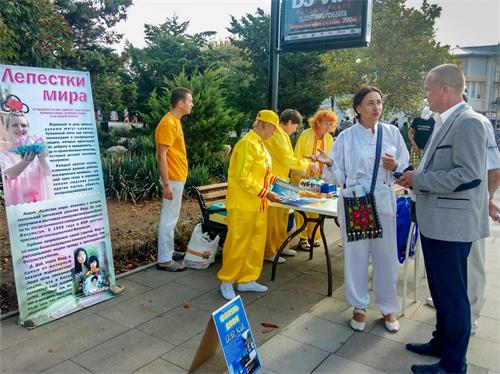 '图4:法轮功学员(中间穿白衣服的女士)向苏达克市政府首脑安德烈·涅克拉索夫(右,穿灰色西服的男士)介绍法轮功,并送给他真相资料。'