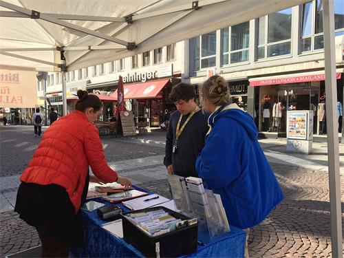 '图1~2:不同族裔的民众在信息台前认真听取法轮功学员讲述中共迫害法轮功的真相,并签名反迫害'