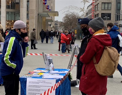 '图1~4:过往民众在法轮功学员的信息台前了解中共的迫害,和学员交谈了解事实真相。'