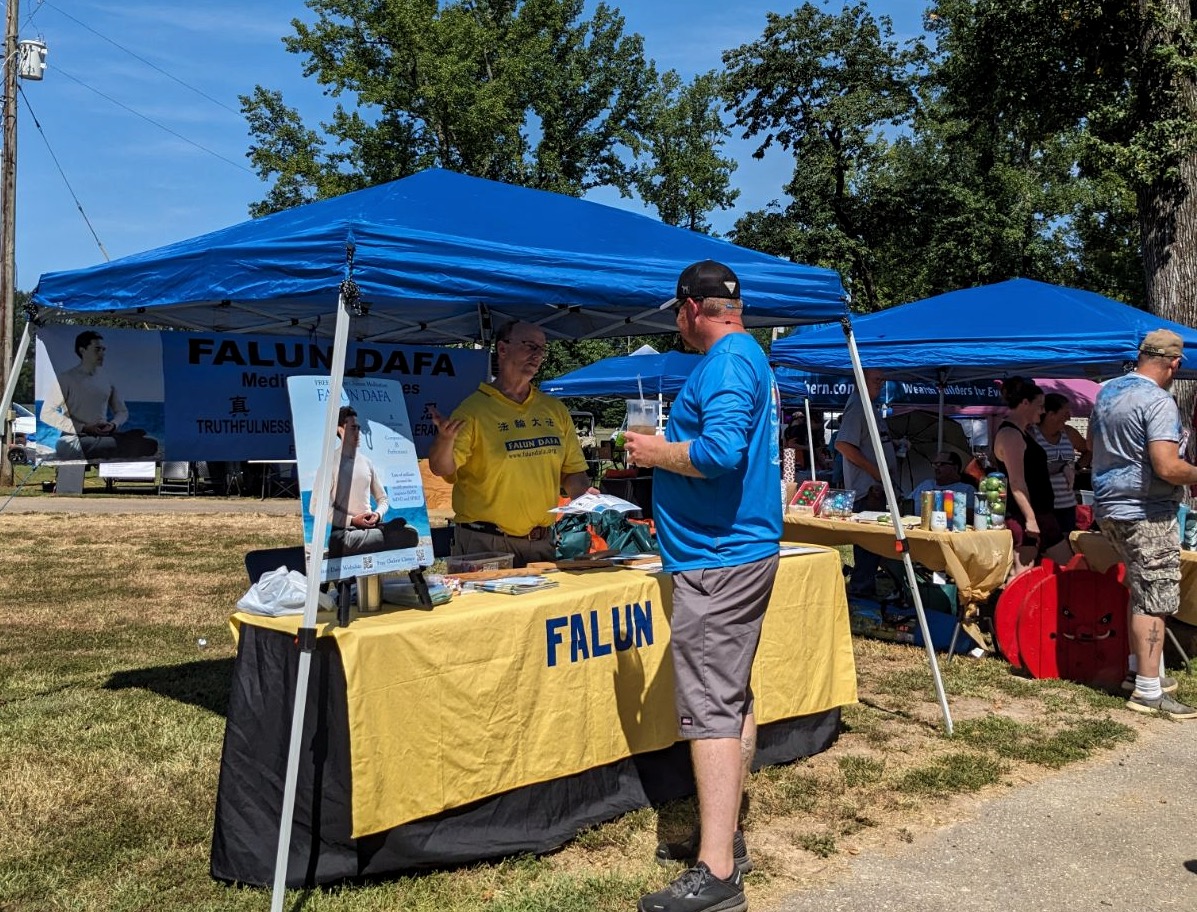 图2:展位中的法轮功学员正在给这位男士(穿蓝色上衣者)介绍法轮功及其真相。