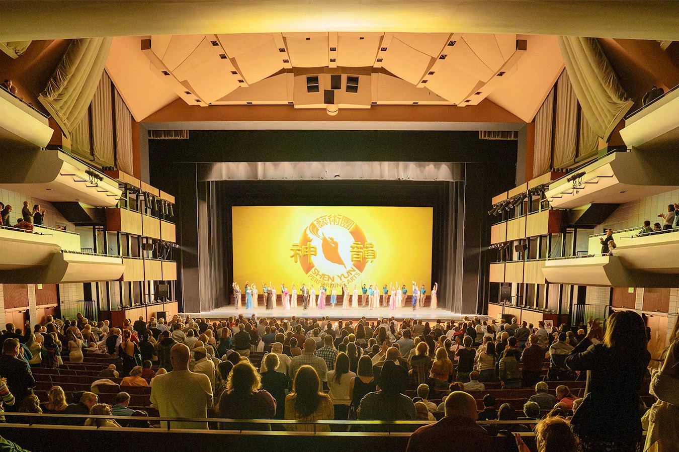 '图10:二零二五年三月二十八日,神韵国际艺术团在科罗拉多州科泉市派克斯峰艺术中心(Pikes Peak Center for the Performing Arts)举办了首场演出。演员谢幕时,全场观众起立鼓掌,人人脸上洋溢着兴奋的表情。'