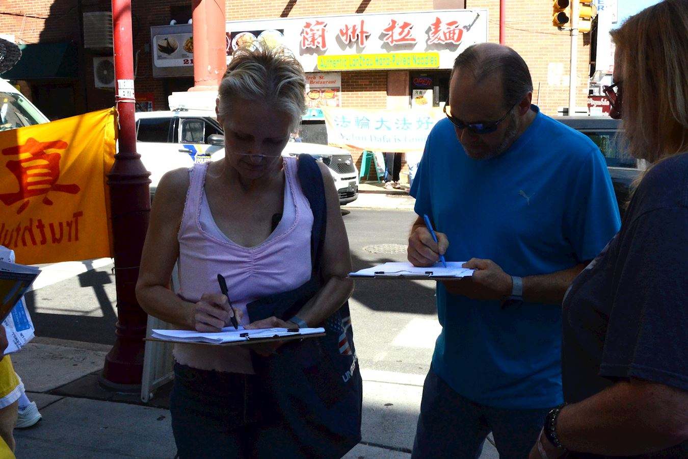 '图11:二零二五年八月三十日在费城唐人街,企业主珍·布尔克(左)在制止中共迫害法轮功的征签表上签字。'