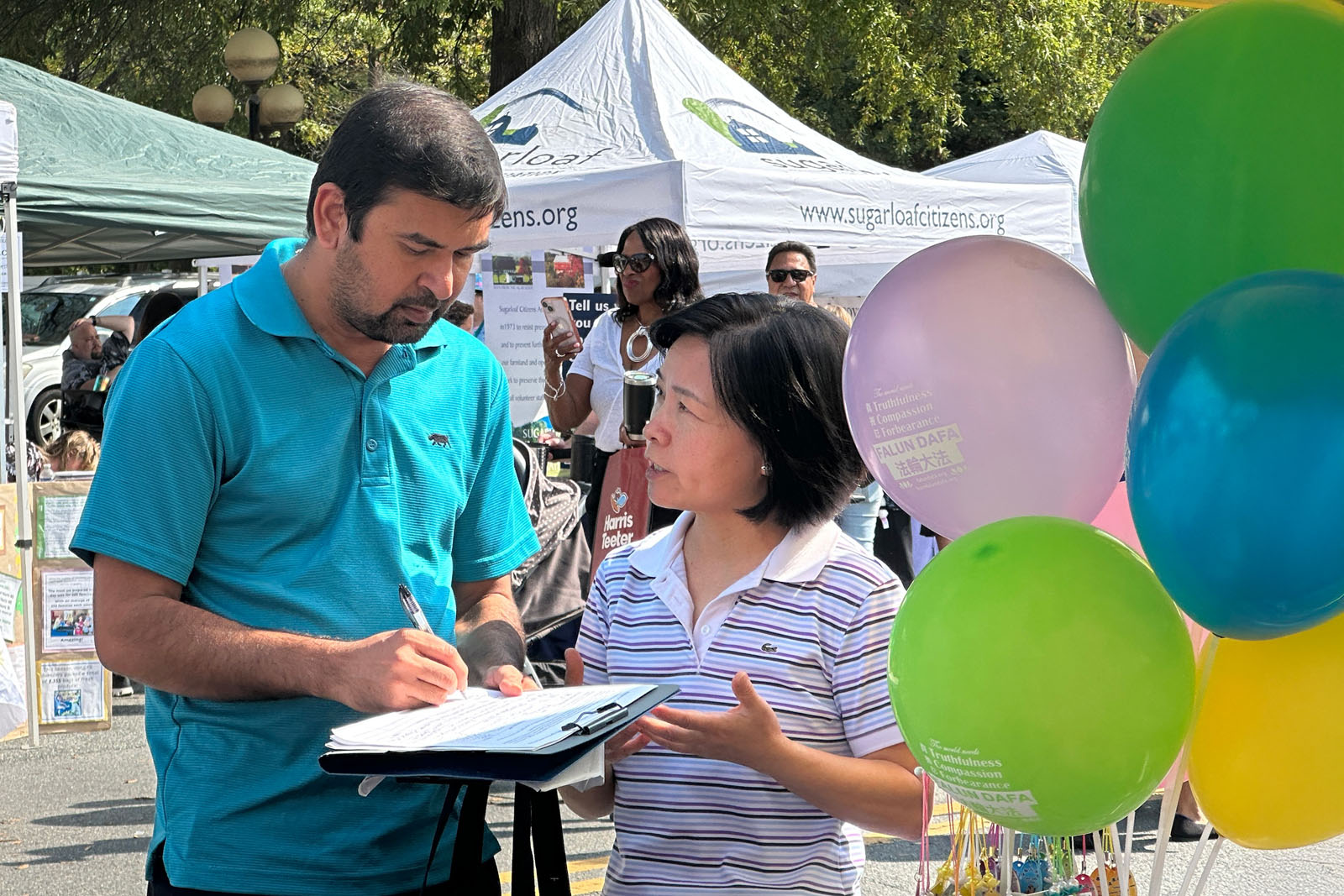 图11:普尔斯维尔当地居民帕特尔(左)听一位法轮功学员(右)跟他讲述真相后,在请愿书上签名,反对中共活摘法轮功学员器官。