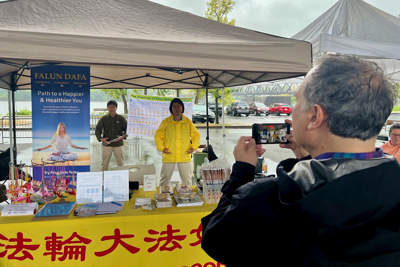 '图8:鲍勃(右前)几年前购买了《转法轮》,当天在法轮功展台认真的录下了法轮功学员的炼功动作。'